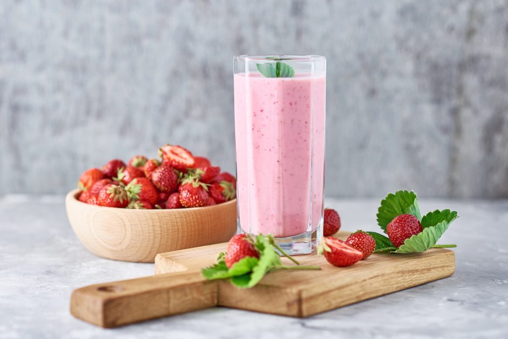 Strawberry milk shake in a glass jar and fresh strawberries with leaves