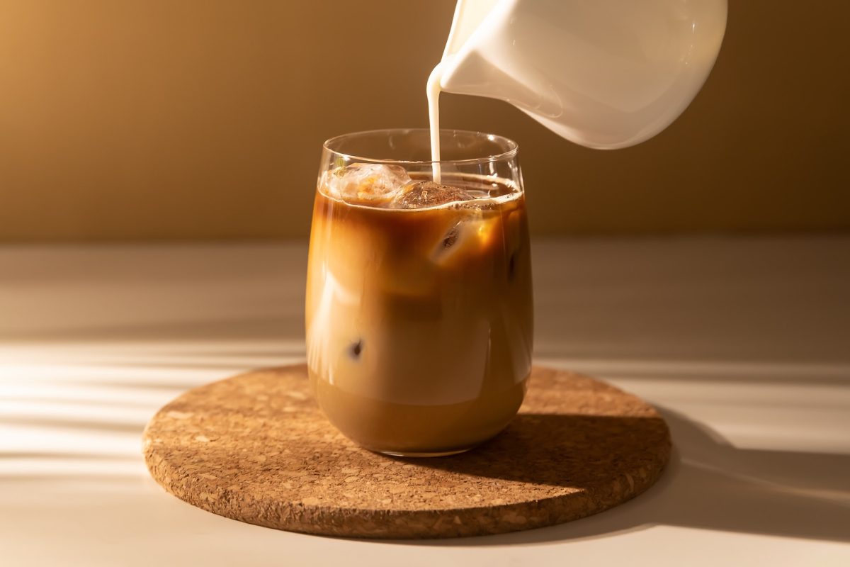 Milk cream is poured into a iced coffee. Coffee cold brew drink with ice and milk.